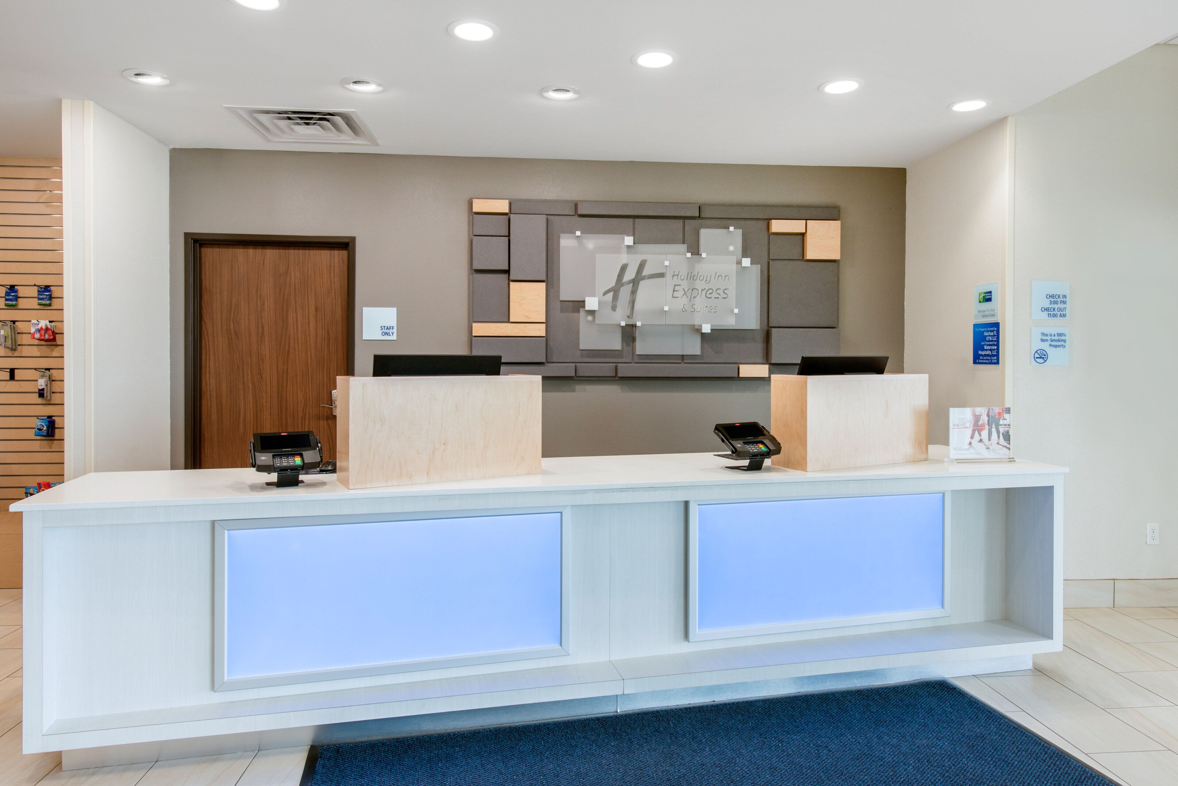 Een receptiebalie van een hotel met een modern ontwerp, een digitaal incheckpunt en een wandbord met de naam van het hotel.