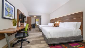A hotel room with a desk, two beds, a chair, a TV, and a colorful rug.