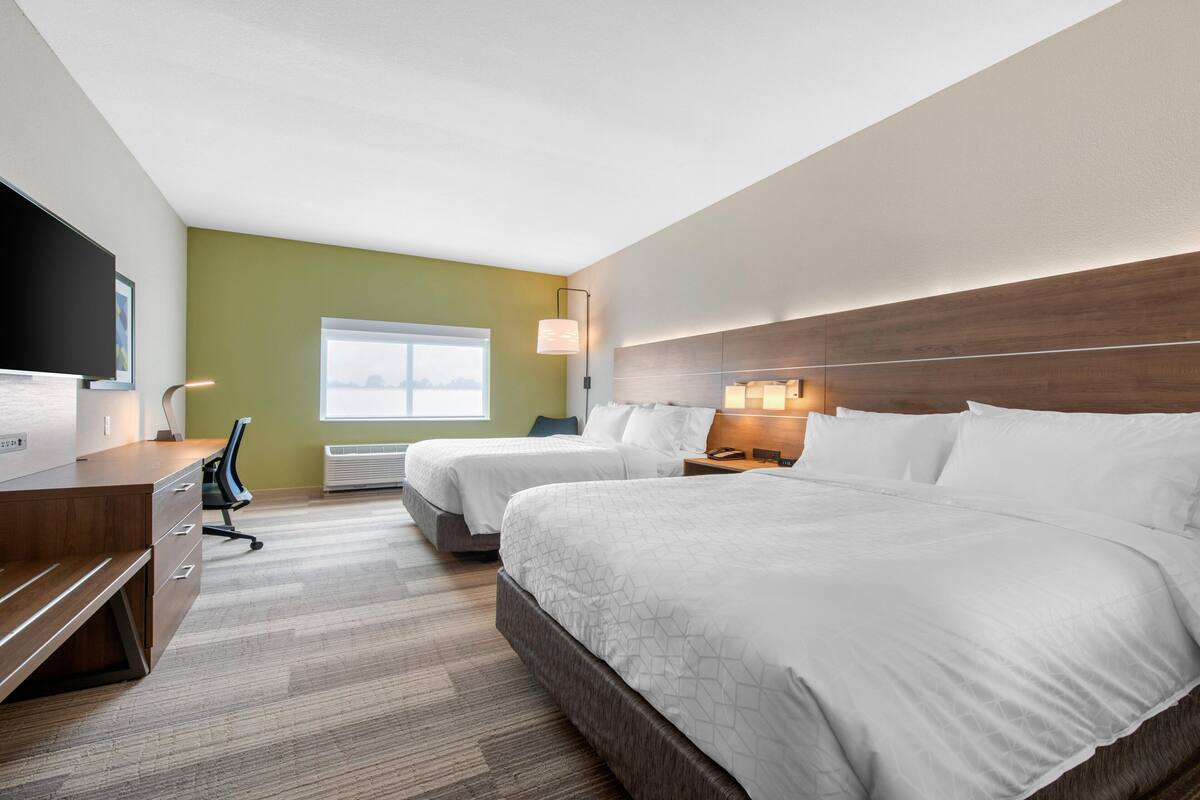 A hotel room with two beds, a desk, a chair, a TV, and a window.