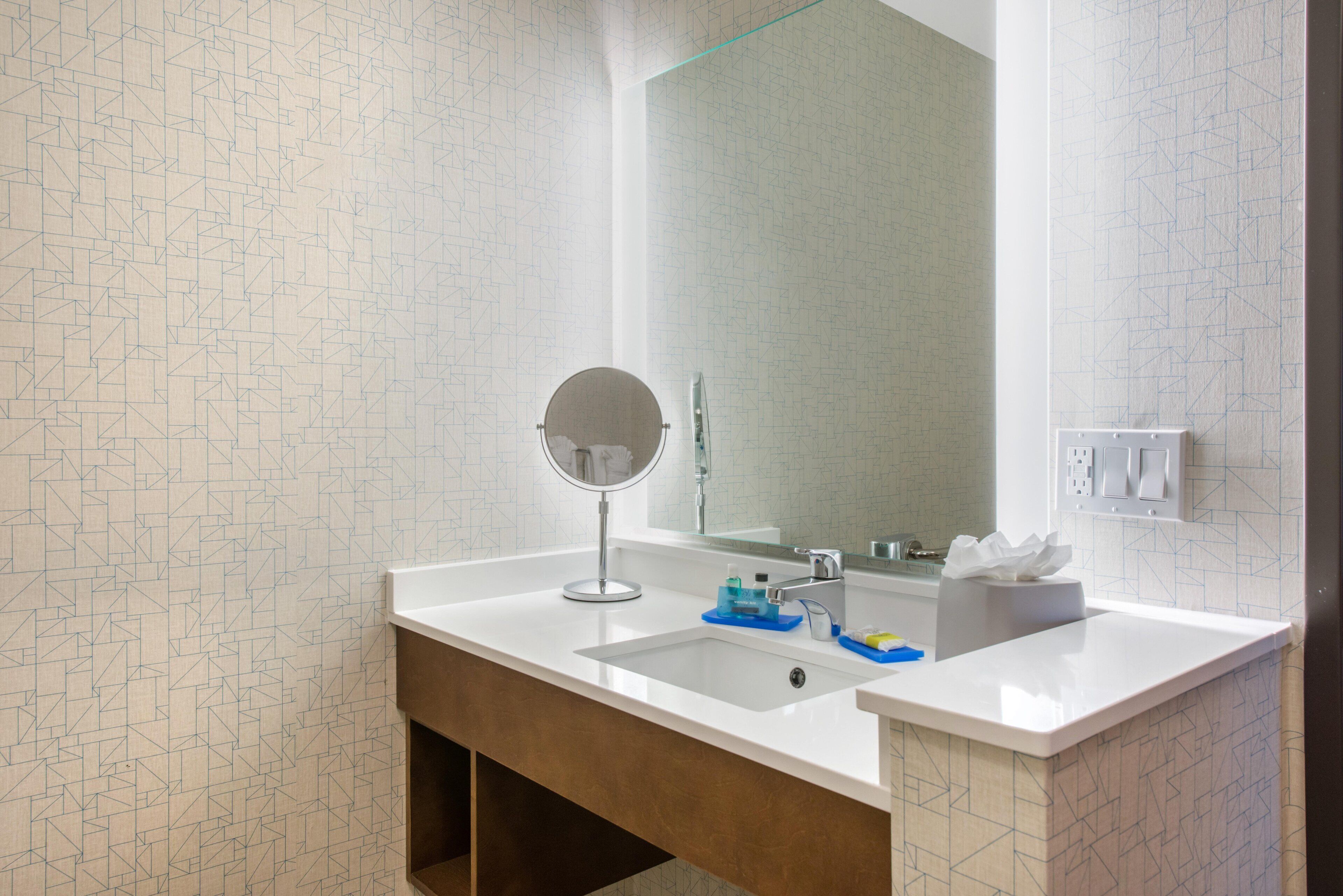 A bathroom with a white sink, a round mirror, and a large mirror above the sink.