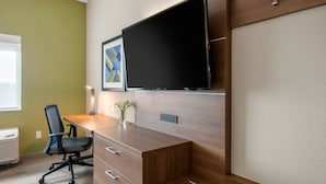 Un espace de bureau moderne avec un bureau en bois, une chaise de bureau noire, un téléviseur à écran plat fixé au mur et une œuvre d'art abstraite encadrée accrochée au mur.