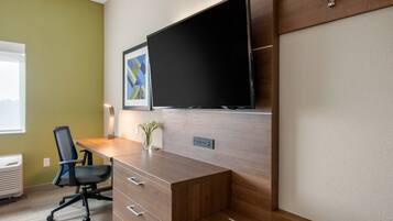 A modern office space with a wooden desk, a black office chair, a mounted flat-screen TV, and a framed abstract artwork on the wall.
