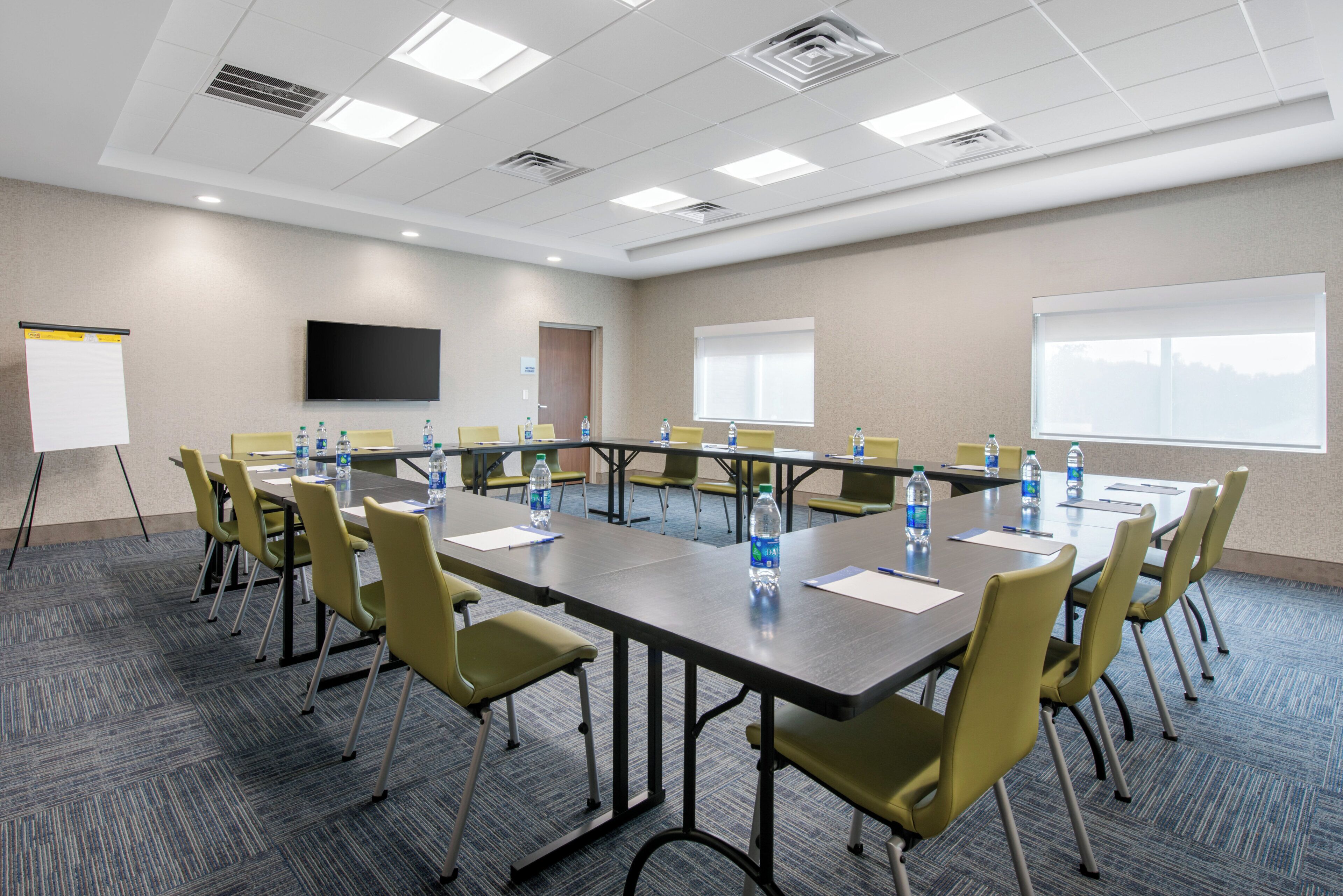 A conference room with a long table, chairs, water bottles, a whiteboard, and a TV screen.