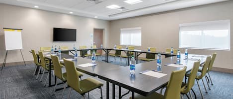A conference room with a long table, chairs, water bottles, a whiteboard, and a TV screen.