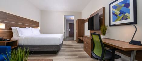 A hotel room with a bed, desk, chair, TV, and a potted plant.