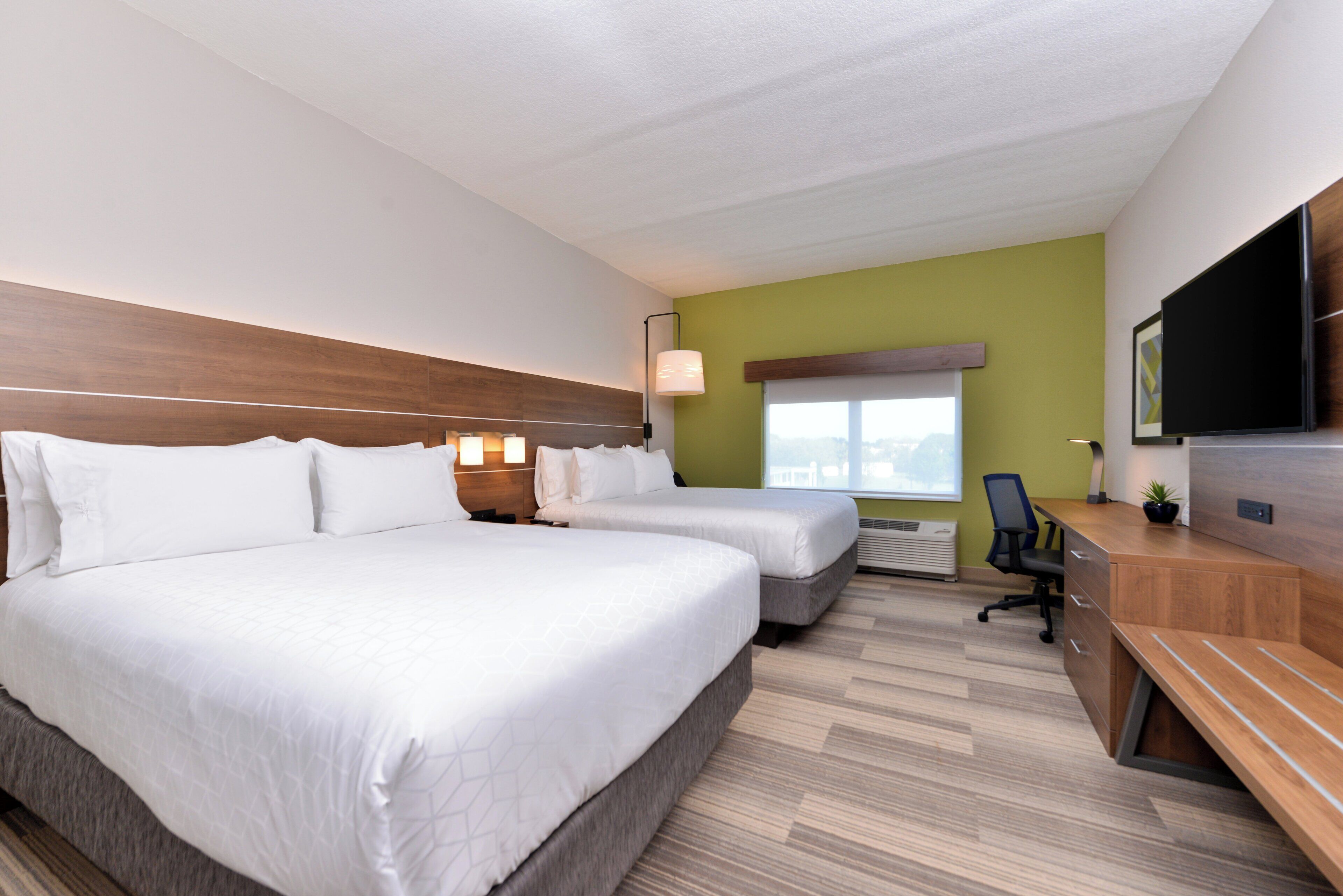 A hotel room with two beds, a desk, a chair, a flat-screen TV, and a window with a view.