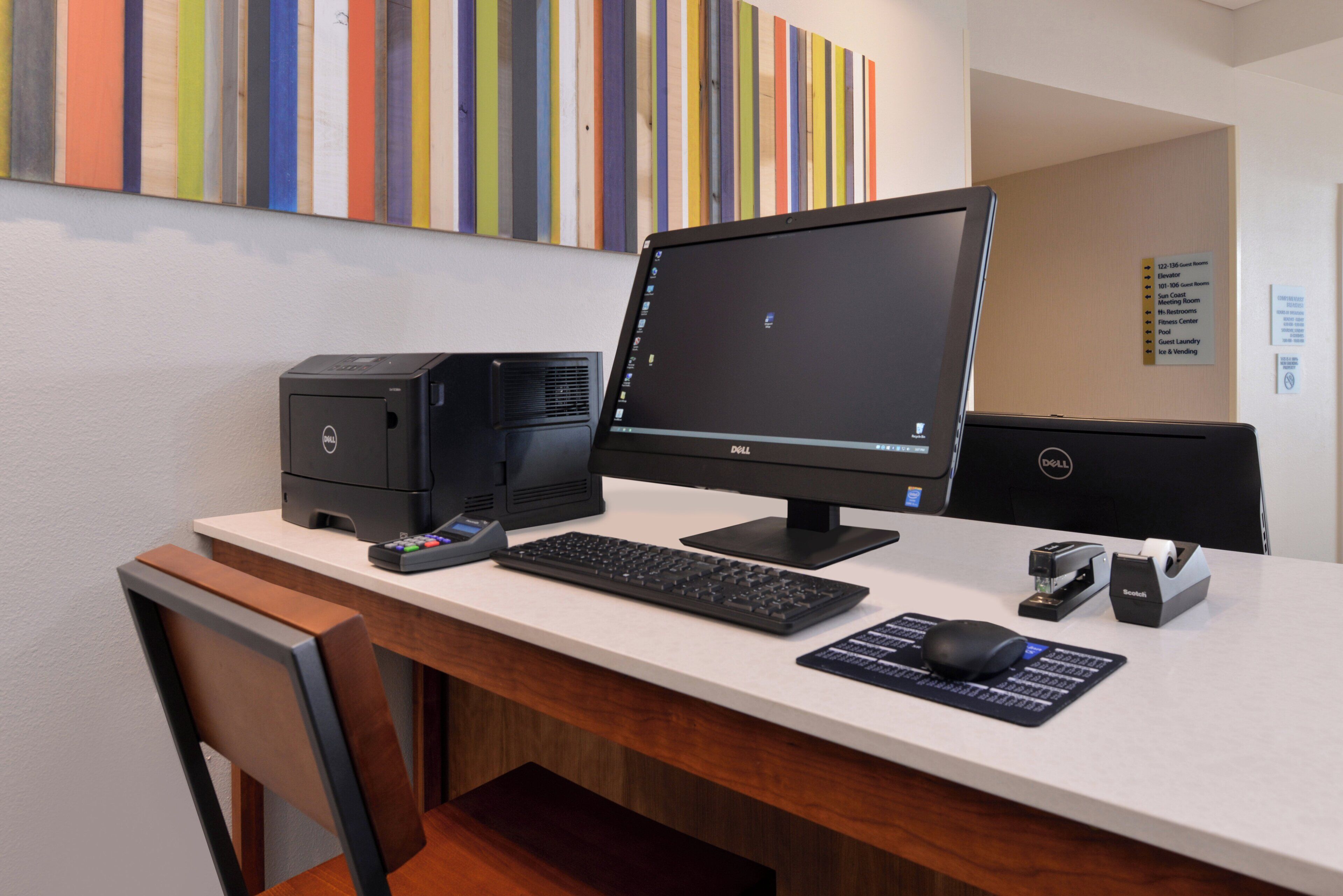 Mostrador de hotel con computadora de escritorio, impresora, teclado, ratón y teléfono.