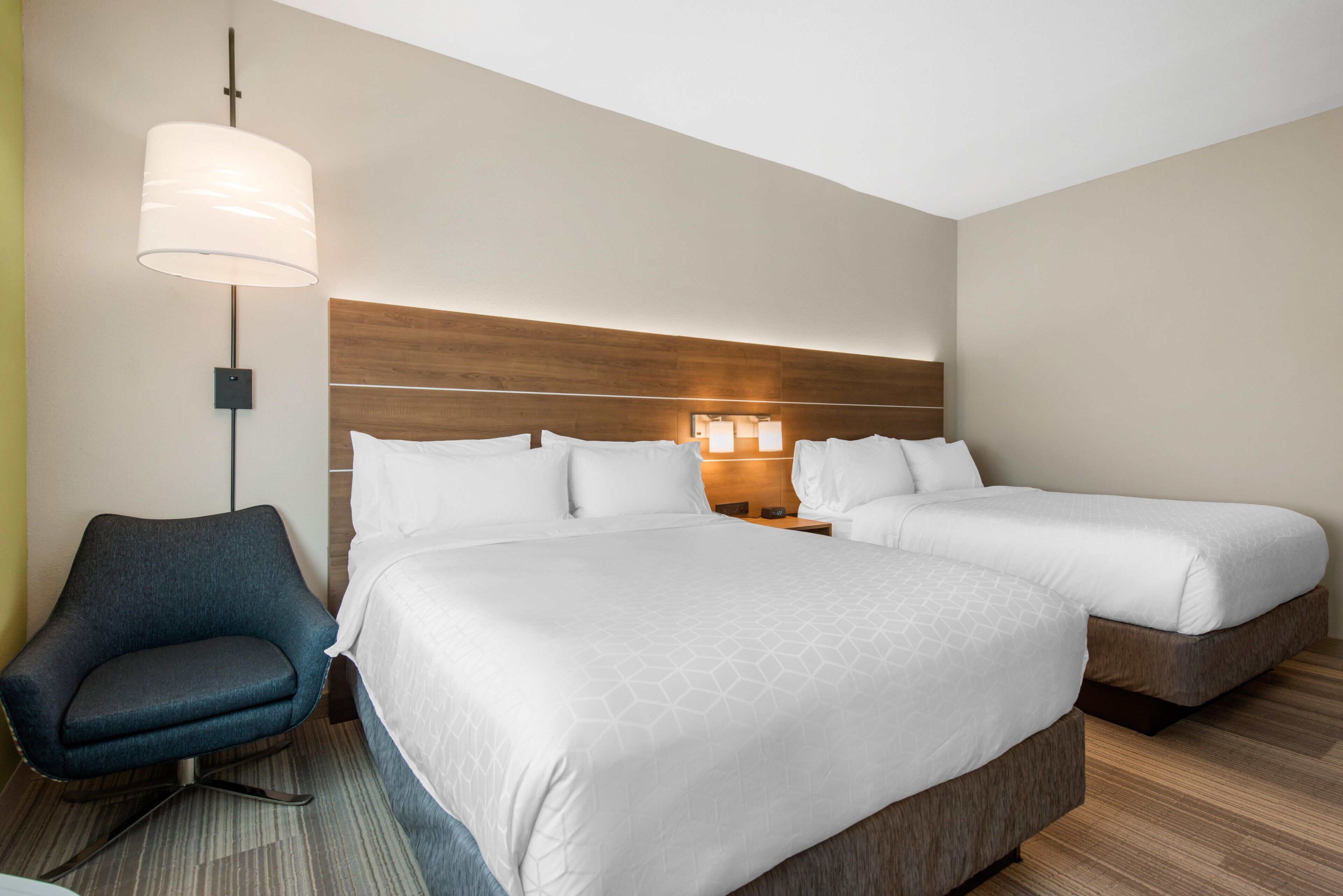 A hotel room with two beds, a chair, a lamp, and a nightstand.