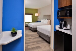 A hotel room with two beds, a microwave, a coffee maker, and a small plant on a shelf.