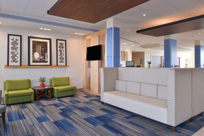 A lobby with a patterned carpet, two green armchairs, a white sofa, a small round table with a plant, and framed artwork on the wall. - Holiday Inn Express & Suites Alachua - Gainesville Area by IHG (Alachua)