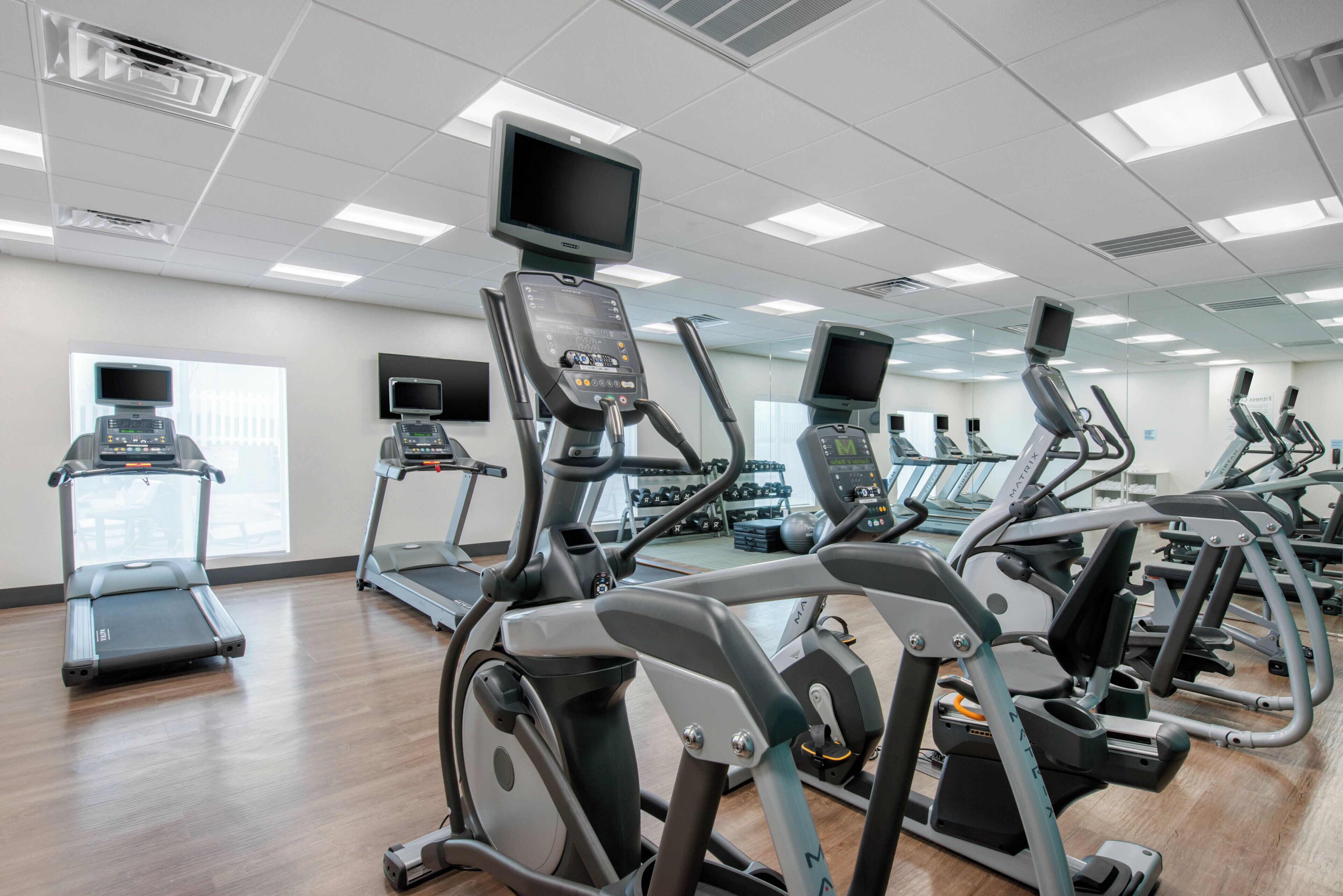 A gym with multiple treadmills and exercise bikes, equipped with digital screens and control panels.