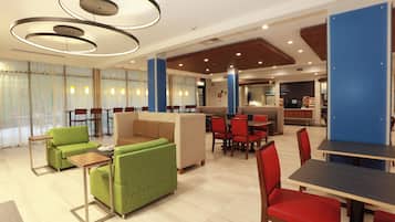A modern hotel lobby with seating areas, a coffee bar, and a reception desk.