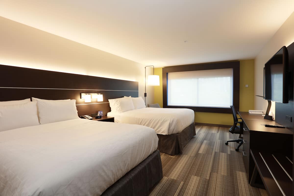 A hotel room with two beds, a desk, a chair, a TV, and a window.