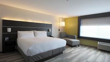 Una camera d'albergo con un letto grande, un comodino, una sedia, una lampada da terra e una finestra.