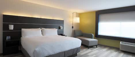 A hotel room with a large bed, a bedside table, a chair, a standing lamp, and a window.