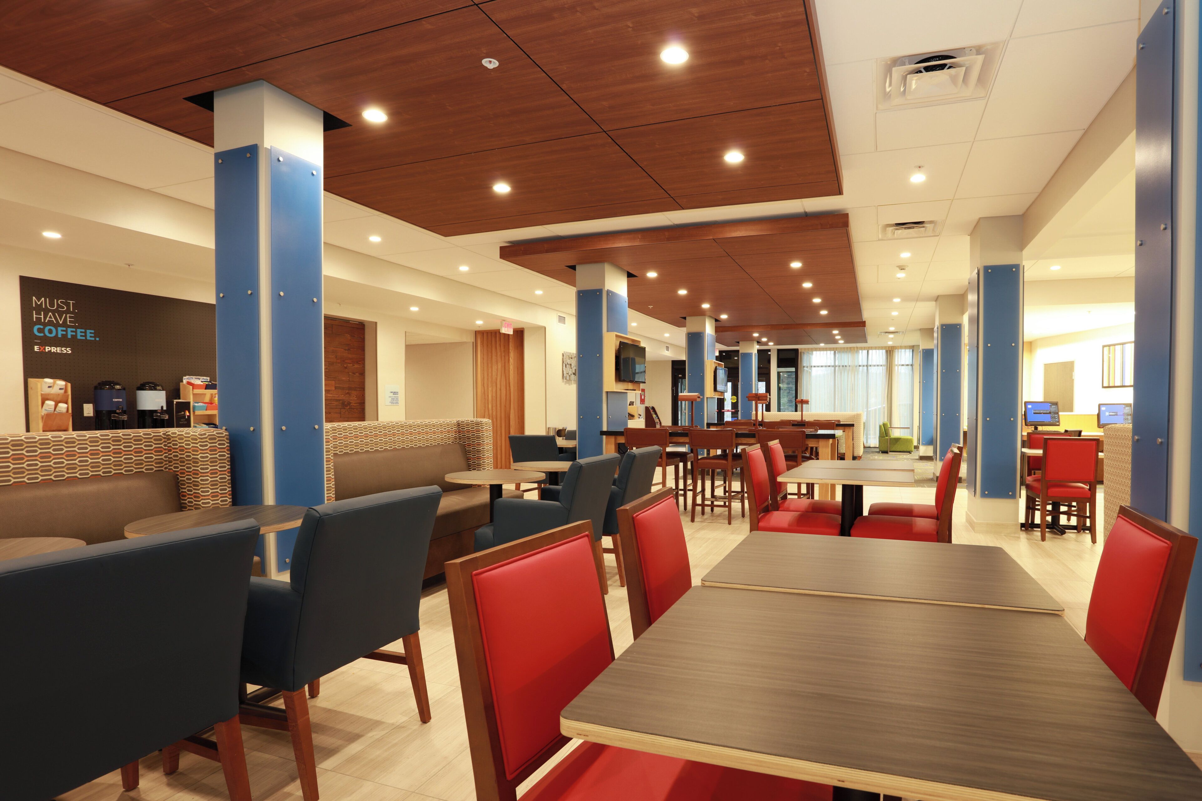 A modern restaurant with booths and tables, wooden ceiling, and blue pillars.