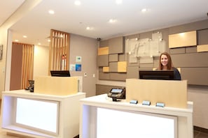 A hotel reception desk with a digital check-in kiosk, a telephone, and a sign indicating check-in times.