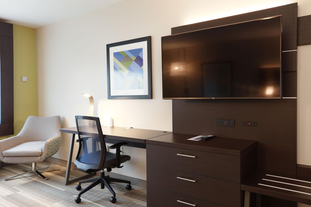 A modern office space with a desk, office chair, and a large flat-screen TV mounted on the wall.