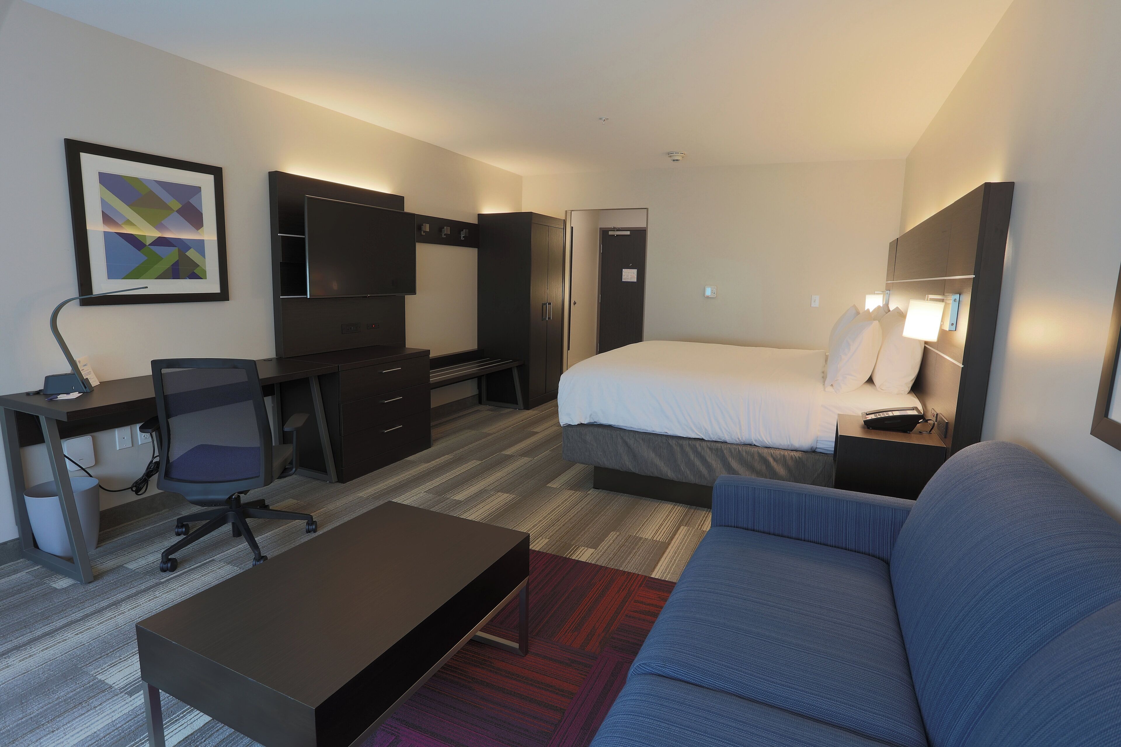 Ein Hotelzimmer mit einem Bett, einem Schreibtisch mit Stuhl, einem Fernseher und einem Sofa.