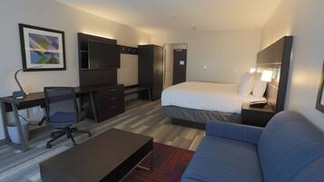 A hotel room with a bed, a desk with a chair, a television, and a sofa.