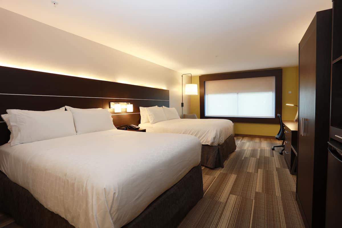A hotel room with two beds, a desk, a chair, a minibar, and a large window.