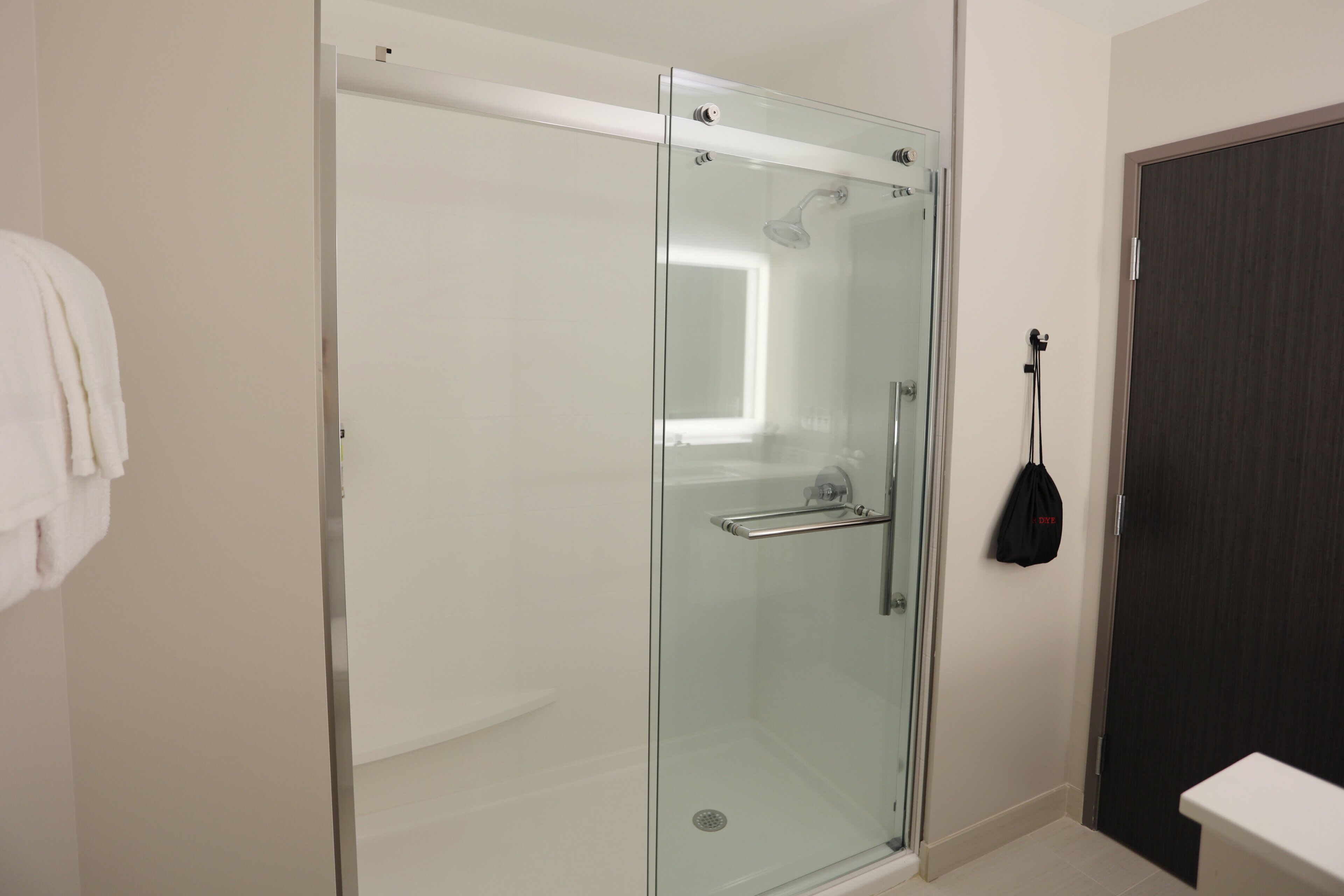 A modern bathroom with a glass-enclosed shower, a white sink, and a dark door.