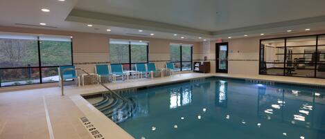 An indoor swimming pool with clear water, marked depth lines, and a seating area with chairs.