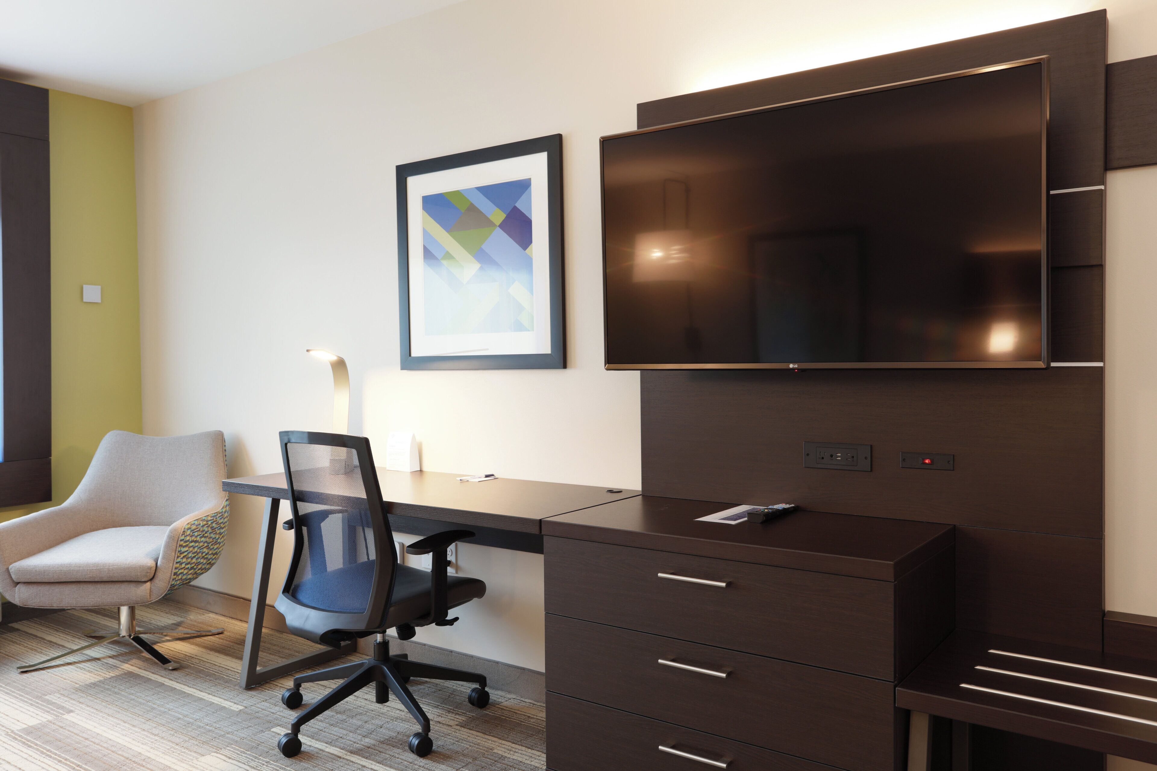 A modern hotel room with a desk, chair, and a flat-screen TV mounted on the wall.