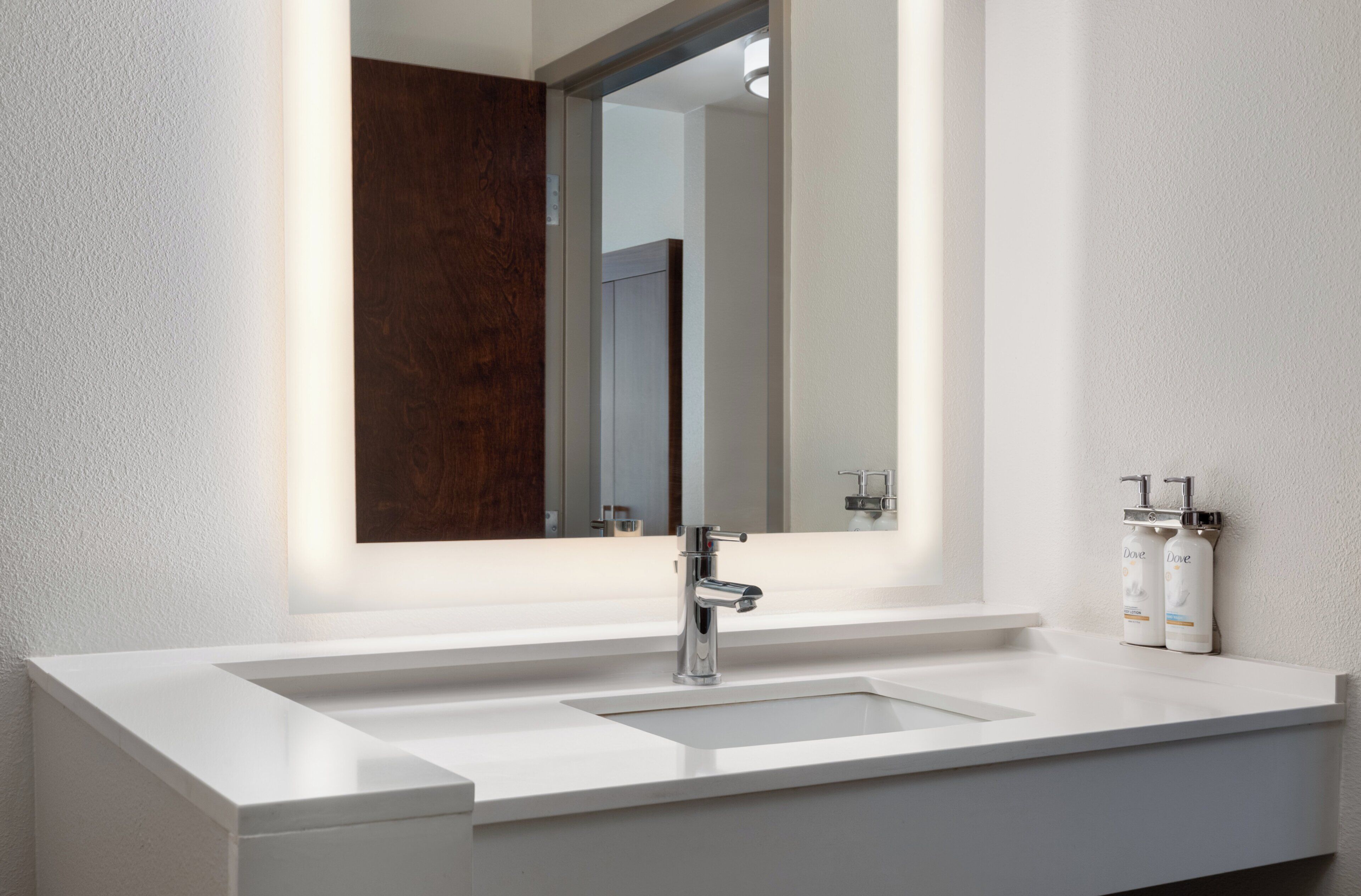 A modern bathroom with a white sink, a large mirror, and two bottles of Dove soap.