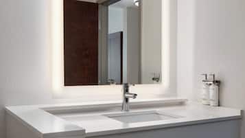 A modern bathroom with a white sink, a large mirror, and two bottles of Dove soap.