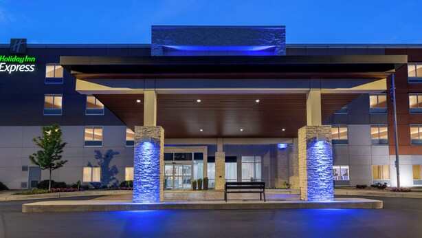 A Holiday Inn Express building with a covered entrance, stone pillars, and a bench in front. - Holiday Inn Express Calhoun South by IHG (Calhoun)