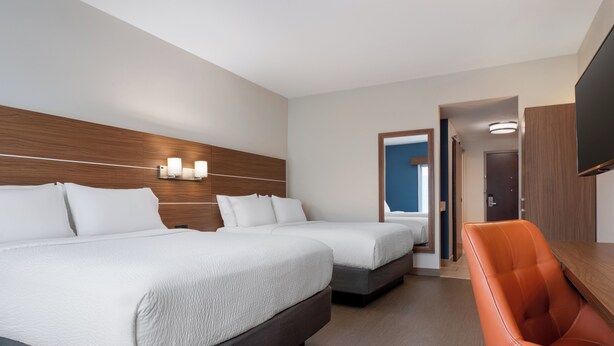 Ein Hotelzimmer mit zwei Betten, einem Holzkopfstück, einem Fernseher und einer Sitzecke.