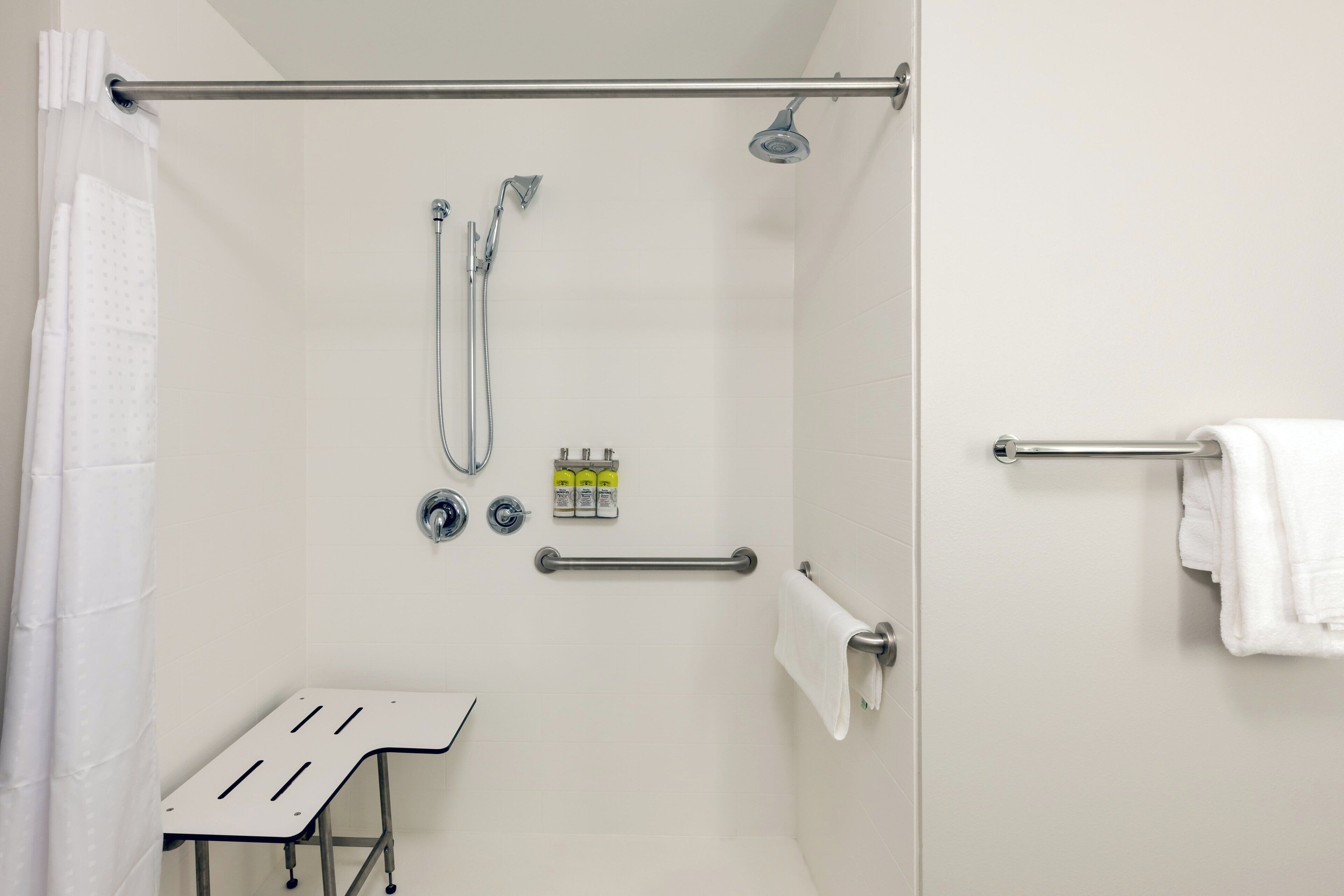 A shower area with a handheld showerhead, a wall-mounted faucet, a towel rack, and a grab bar.
