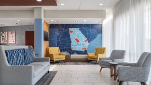 Eine Lobby mit einer Couch, zwei Sesseln, einem kleinen Tisch, einer Wandmalerei mit einer Karte und einem Fernseher an der Wand.