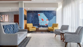 A lobby with a sofa, two armchairs, a small table, a map mural, and a TV on the wall.