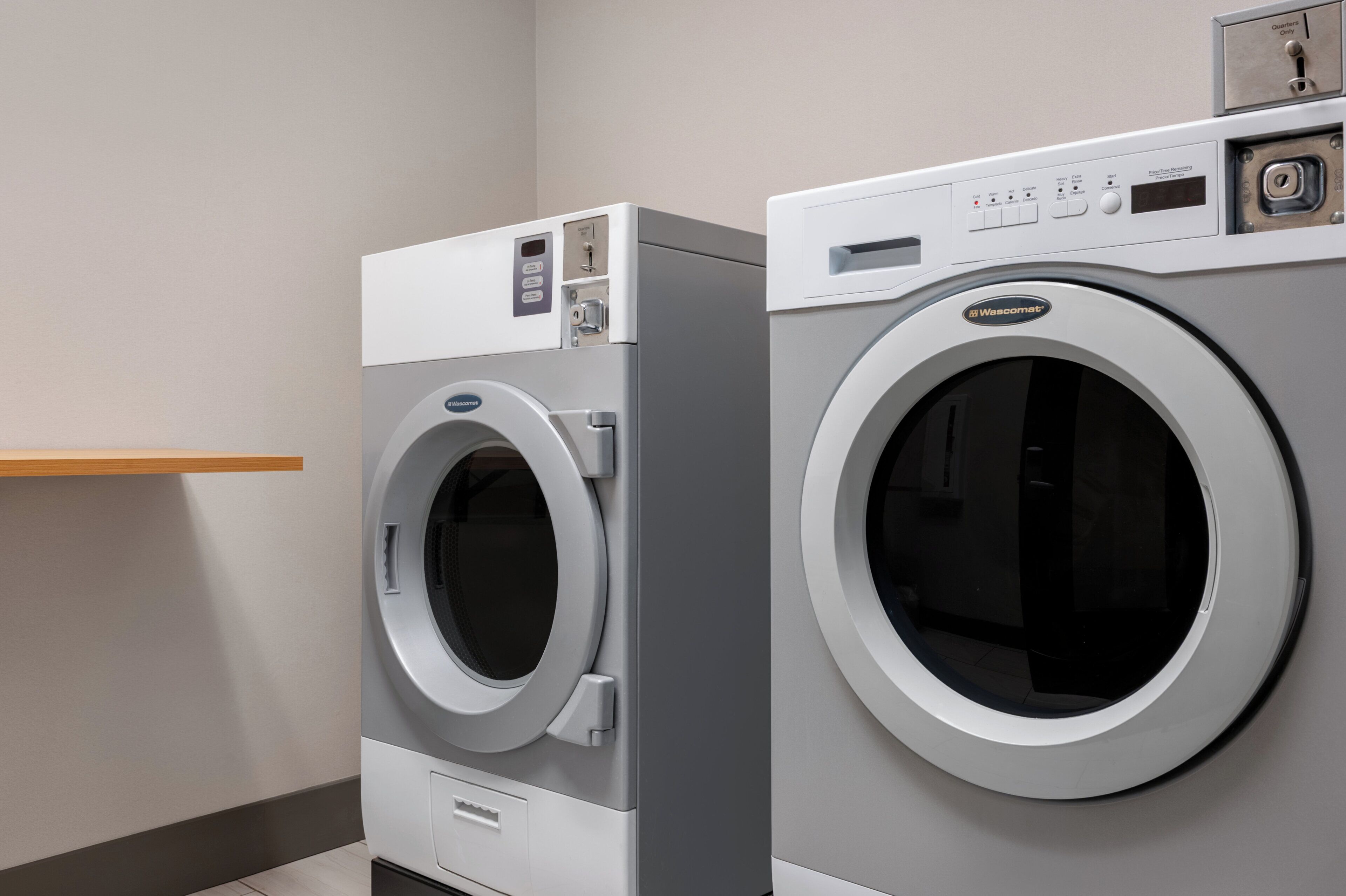 Two front-loading washing machines in a laundry room with a wooden shelf above.