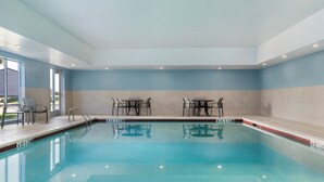 An indoor swimming pool with clear water, surrounded by walls painted in light blue and beige, and equipped with tables and chairs along the poolside. - Holiday Inn Express Calhoun South by IHG (Calhoun)