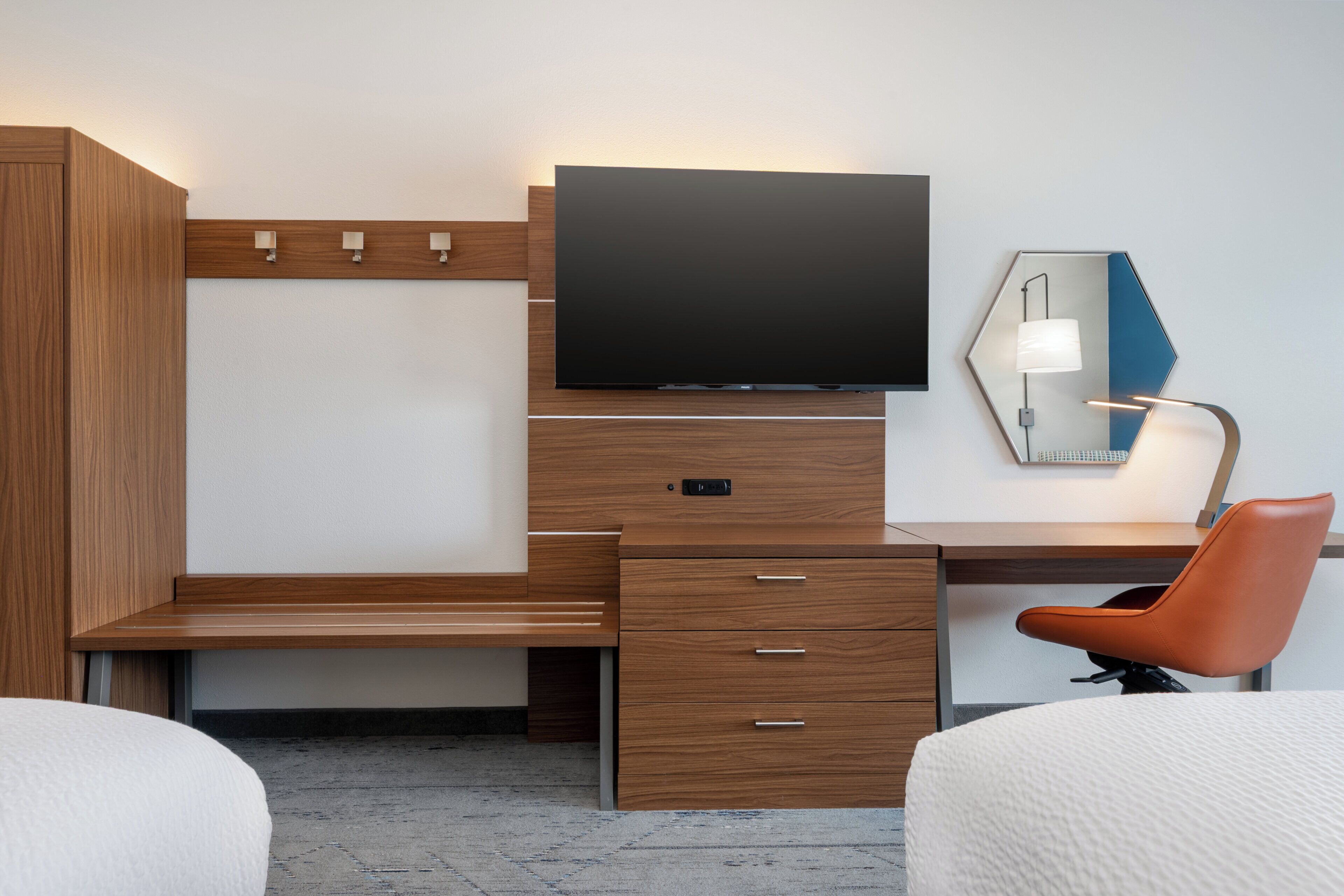 Une chambre d’hôtel moderne avec un bureau en bois, un téléviseur à écran plat, une lampe de bureau et une chaise orange.