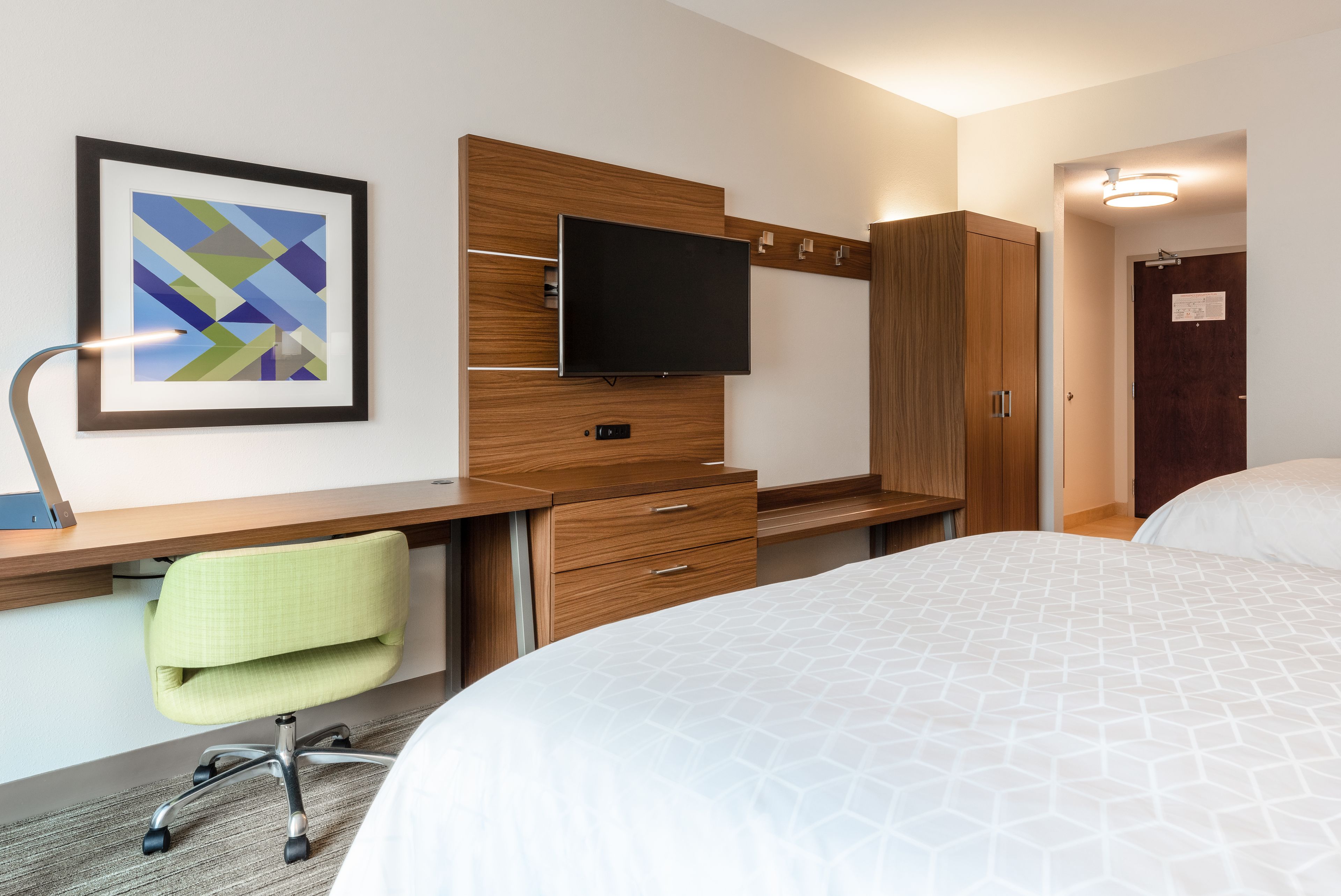 Une chambre d’hôtel comprenant un lit, un bureau avec une chaise, une télévision et une armoire.