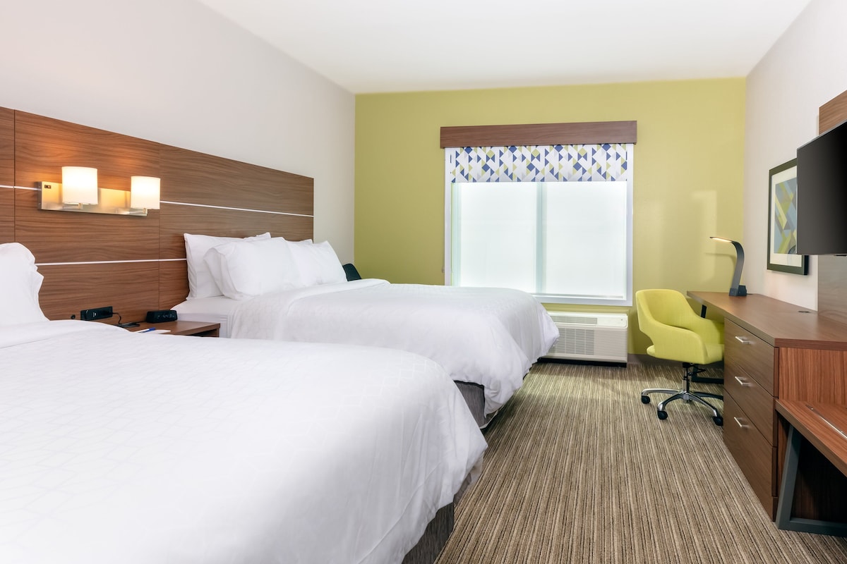 A hotel room with two beds, a desk, a chair, and a television.