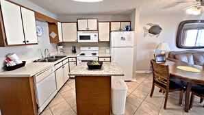A compact kitchen with white appliances, a granite countertop, and a dining area with a brown leather couch. - 👣 Come get your toes in the sand. Lets make a splash! .🌊🐳🐬 (Gulf Shores)