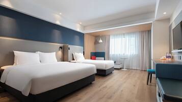 A hotel room with two beds, a desk, a chair, a TV, and a window with curtains.