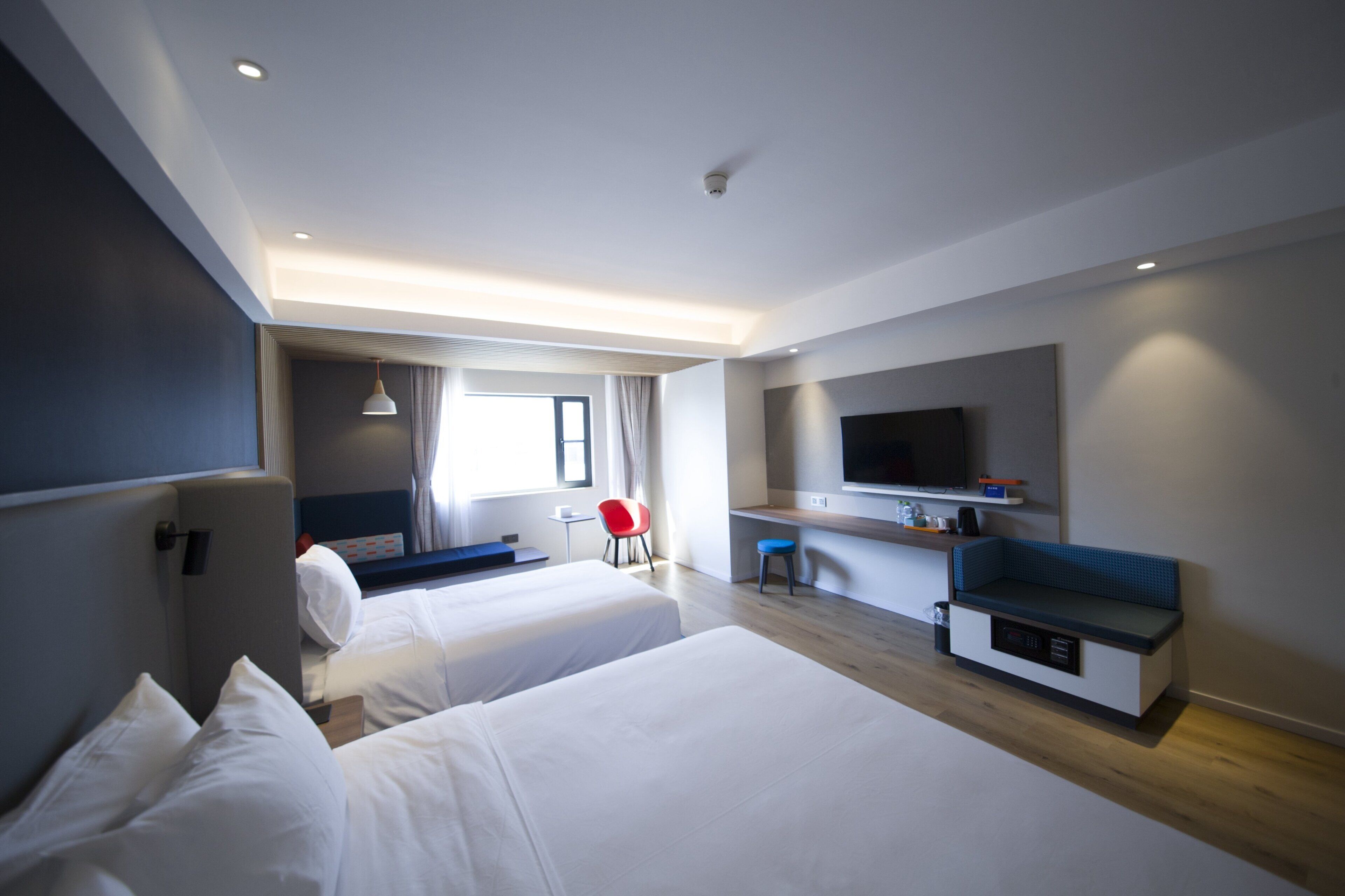 Una habitación de hotel moderna con dos camas, un escritorio, un televisor y una zona de estar.