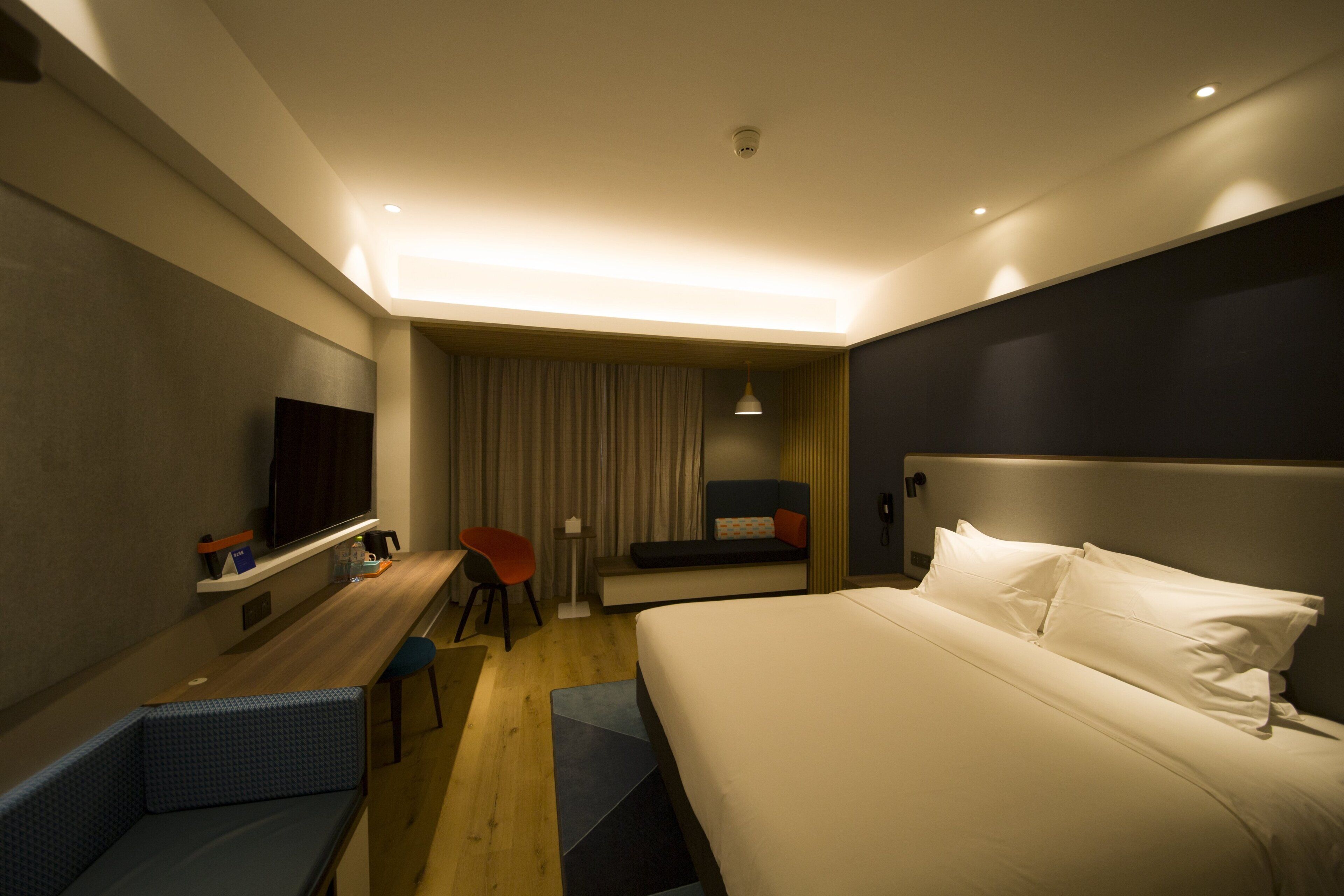 Ein Hotelzimmer mit einem Bett, einem Schreibtisch, einem Sessel, einem Fernseher und einem Vorhang.