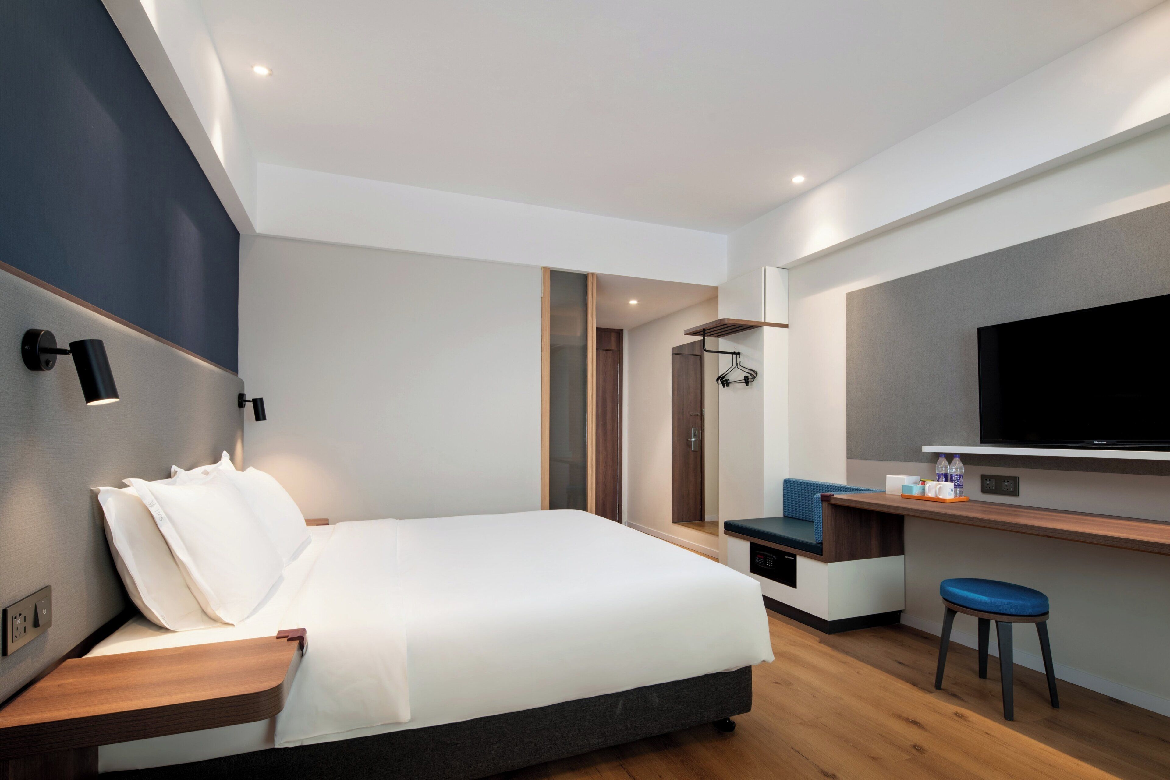A modern hotel room with a bed, a desk, a television, and a bathroom visible through an open door.