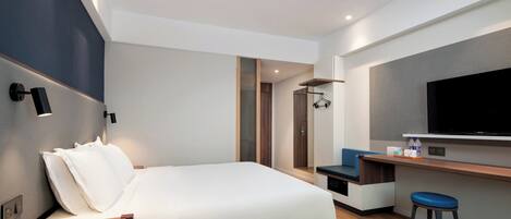 A modern hotel room with a bed, a desk, a television, and a bathroom visible through an open door.