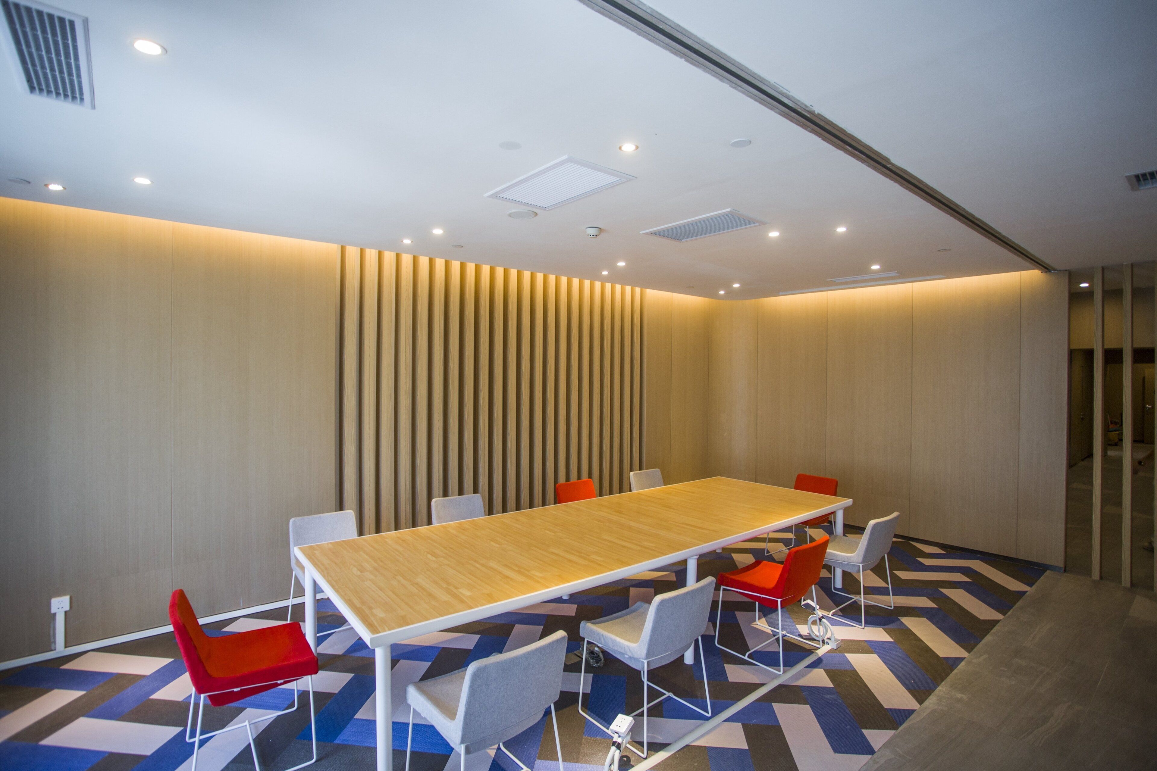 Una sala de conferències amb una taula llarga, diverses cadires i un sòl amb dibuixos.