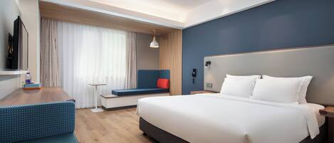 A modern hotel room with a large bed, a seating area, a desk, and a television.