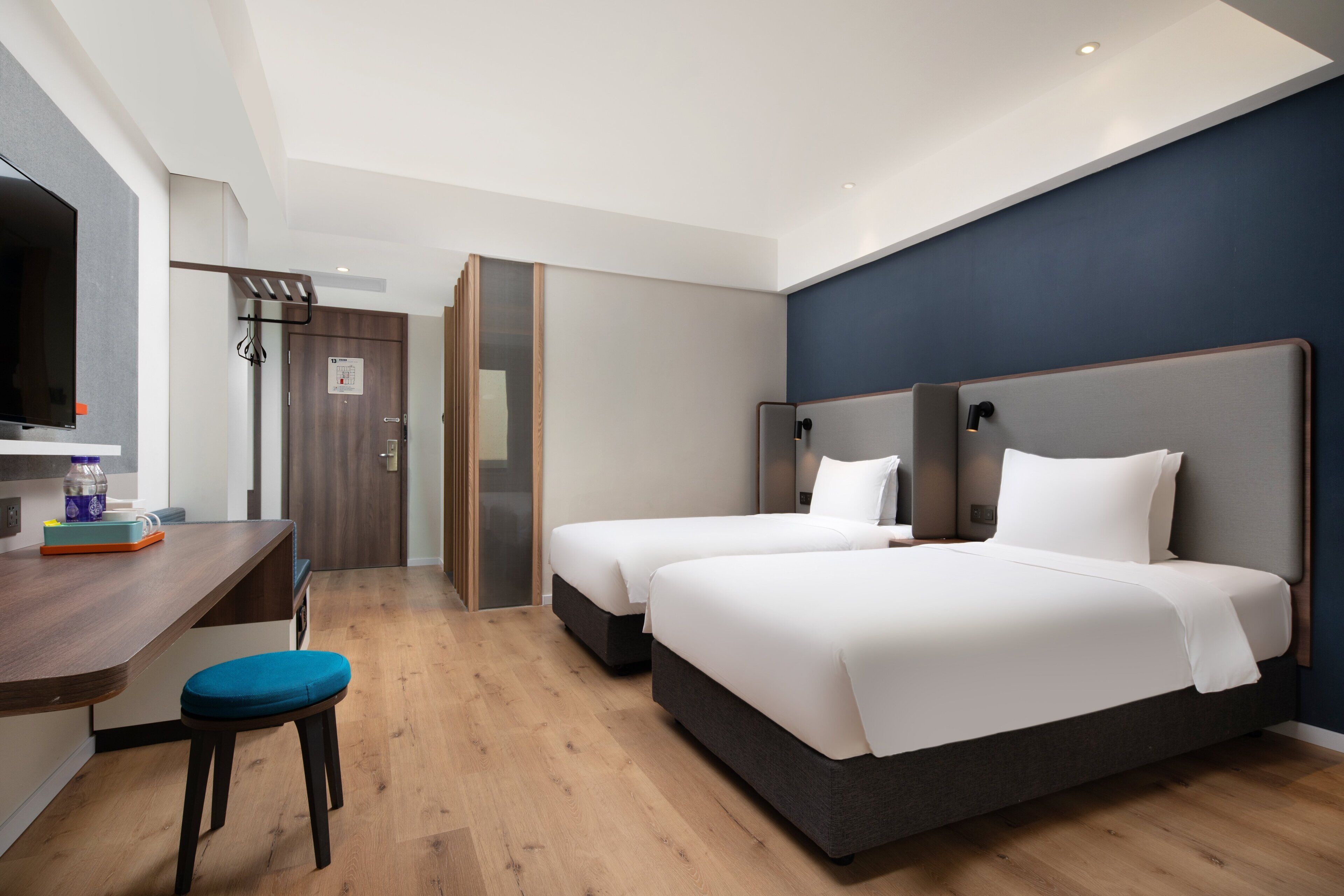 Une chambre d’hôtel moderne équipée de deux lits, d’un bureau avec une chaise et d’une télévision.