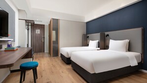 Ett modernt hotellrum med två sängar, ett skrivbord med en stol och en TV.